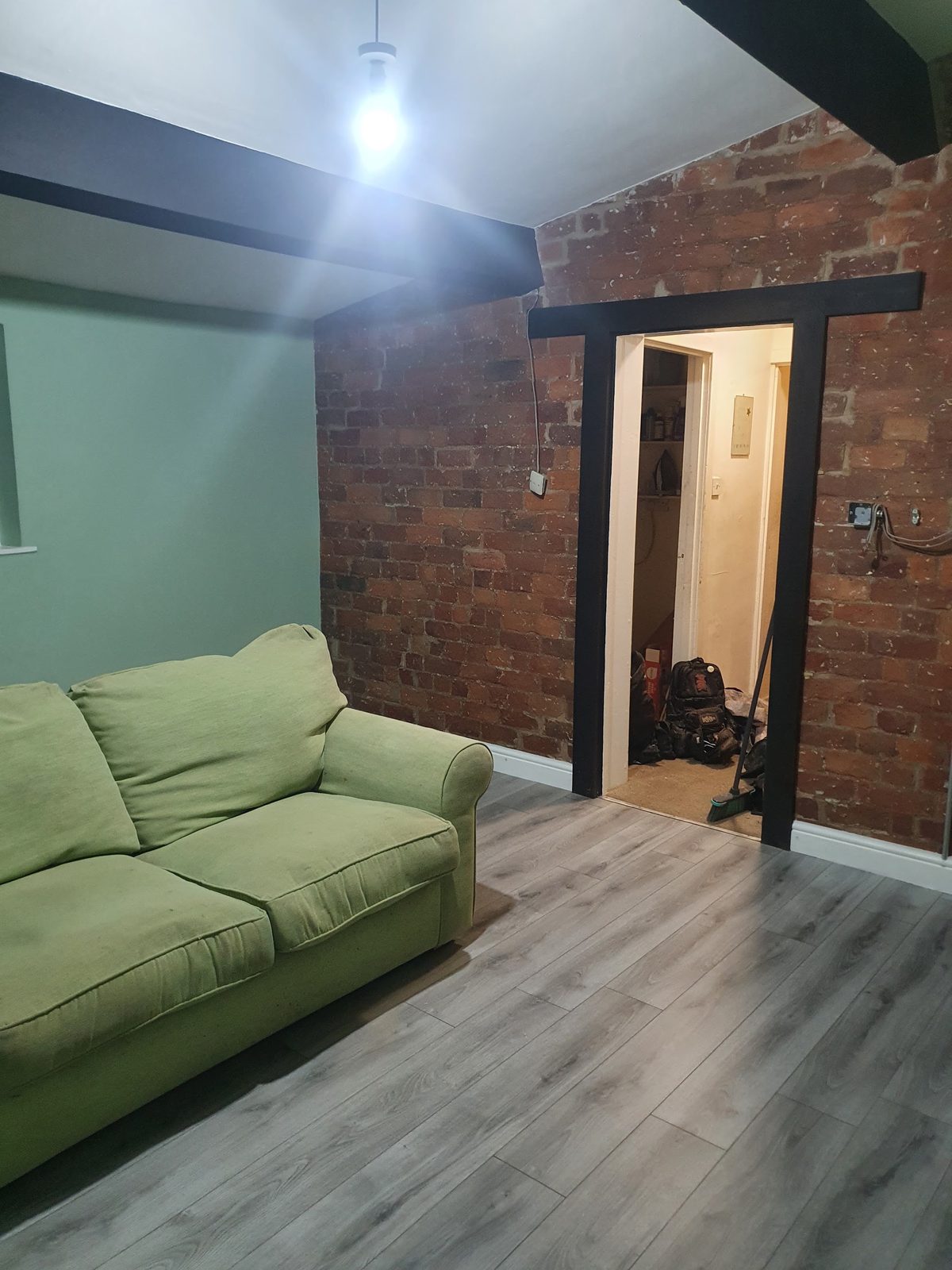 Living room with an exposed red-brick feature wall, black-framed doorway and grey laminate floor