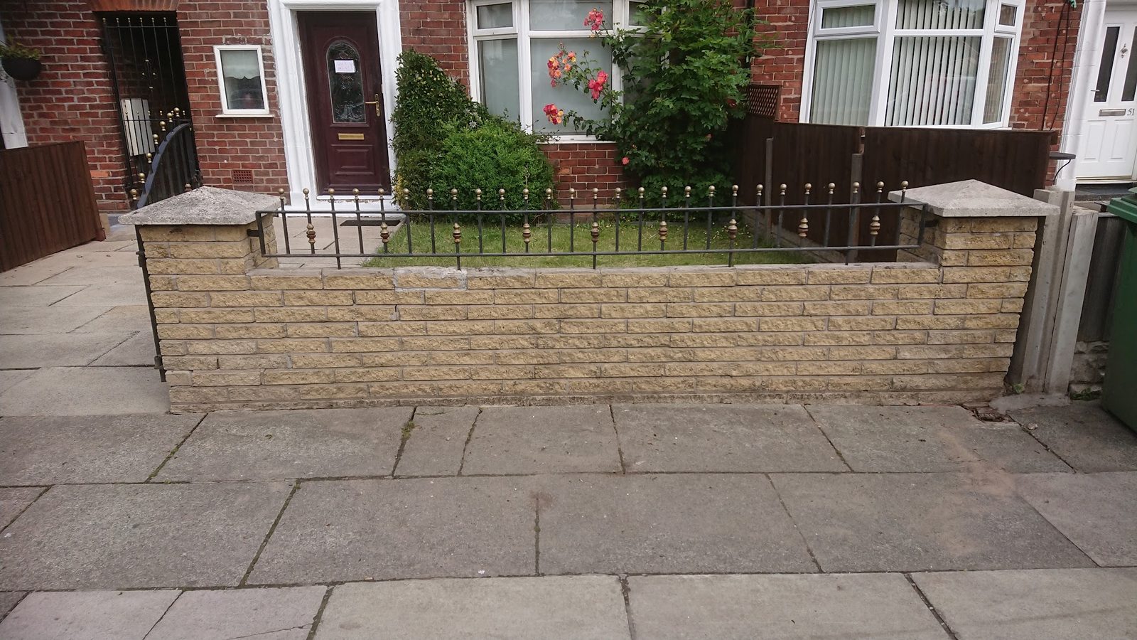 Front garden wall with black railings and new paving outside a red-brick house