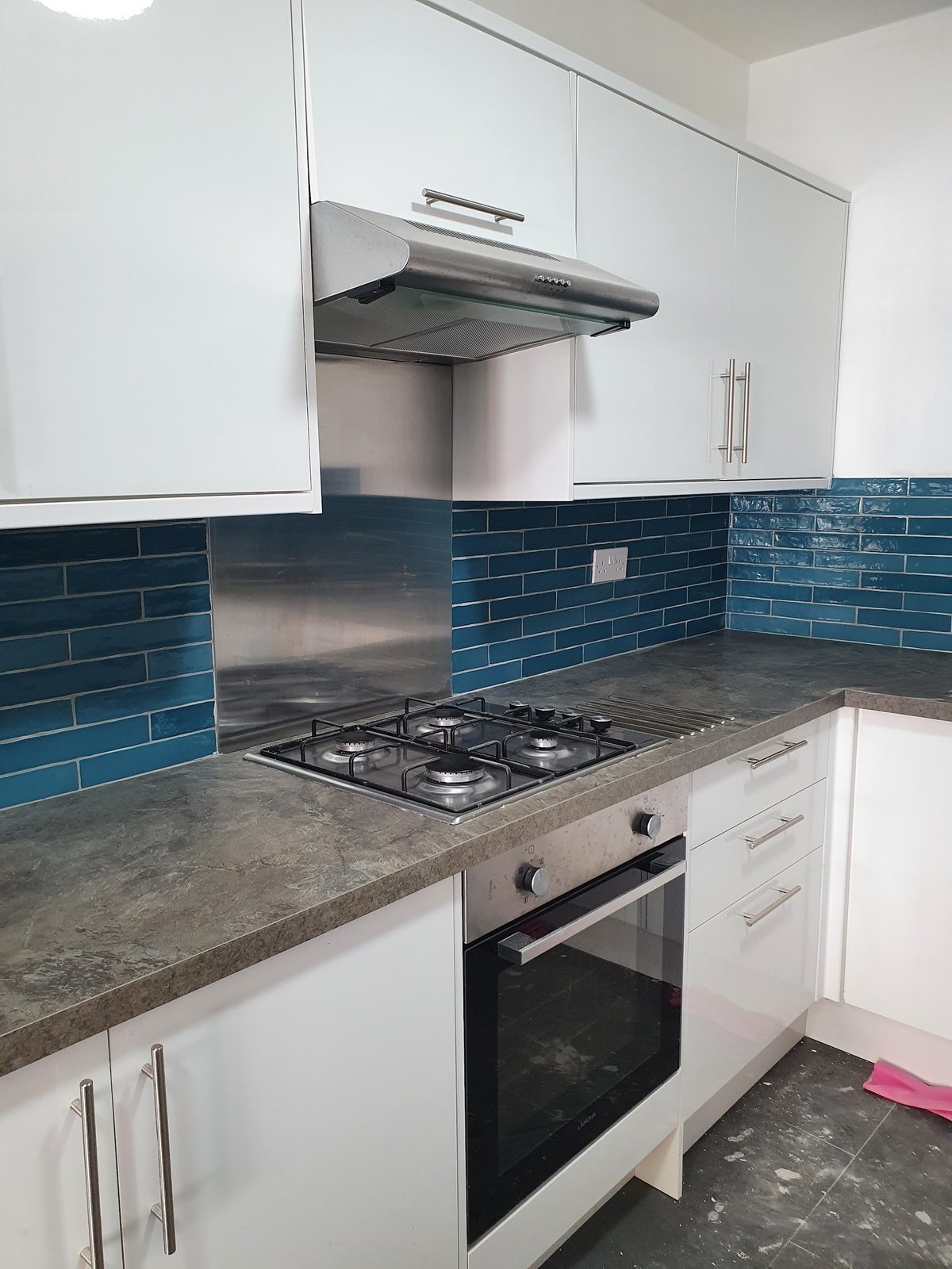 Fitted kitchen with white gloss units, teal metro tile splashback and a gas hob