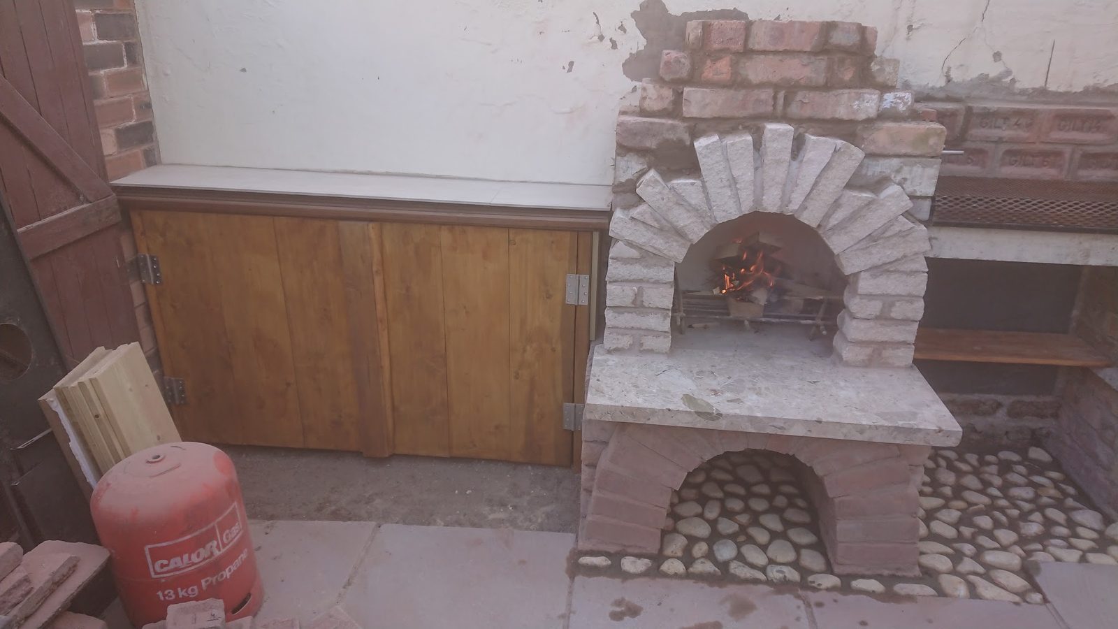 Brick-built outdoor oven with a cobbled base next to a timber storage cupboard