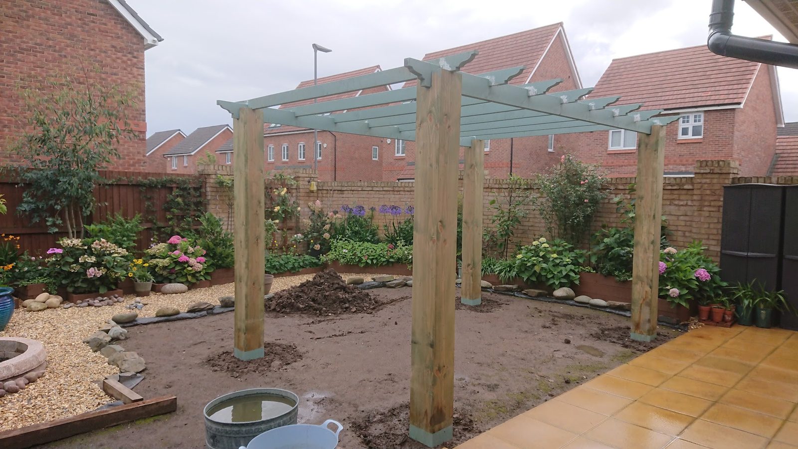 New timber pergola going up in a garden with gravel and planted borders